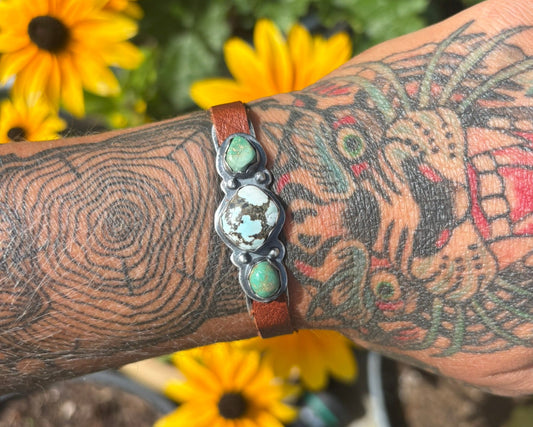 Tattooed arm wearing a bracelet with flowers in the background