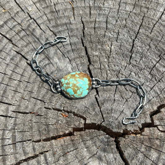 handmade turwuoie and silver bracelet featuring handmade chain and clasp, silver shot detials on both sides and loops for the chain sitting on a wood cut round stump