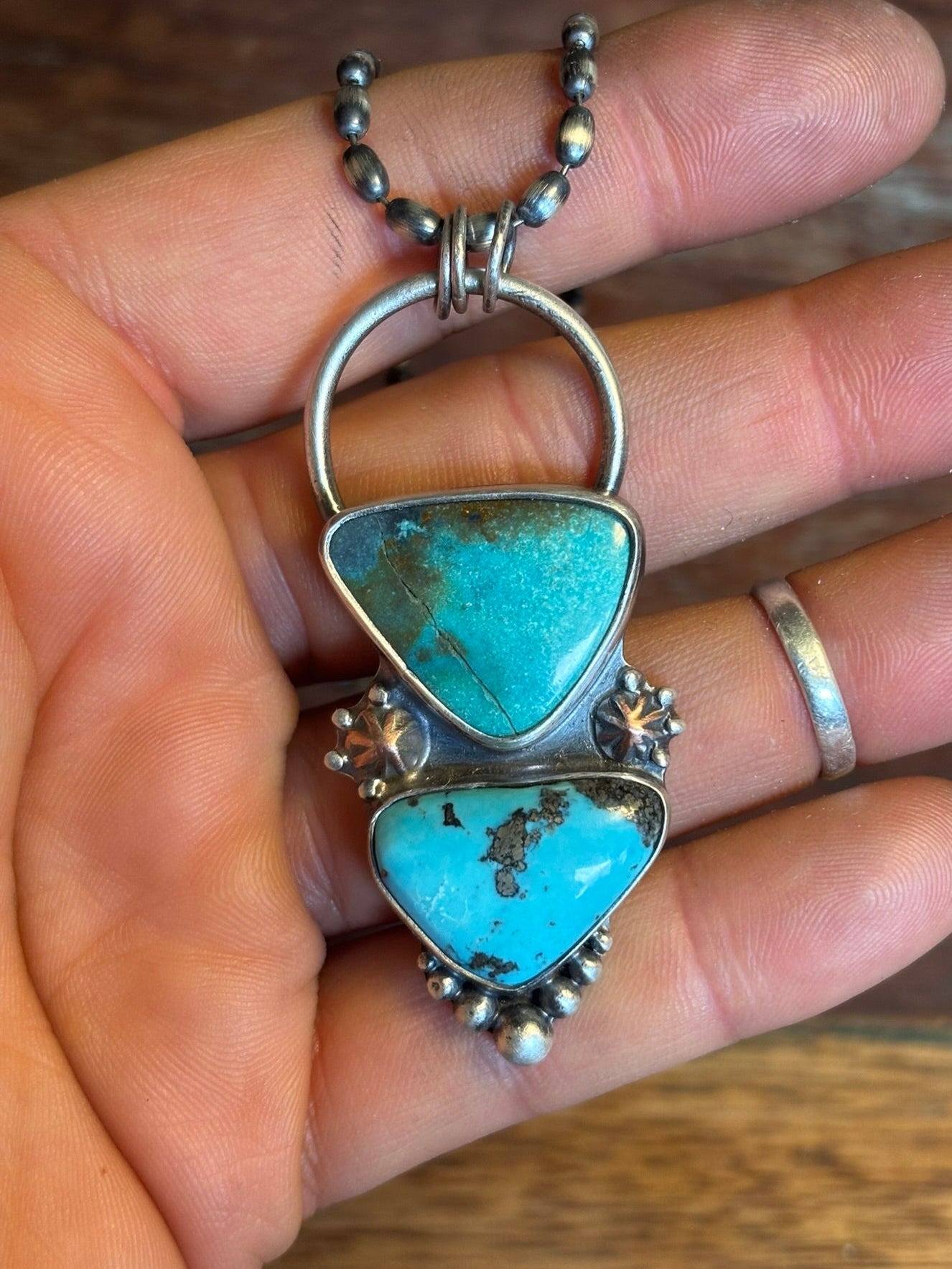 Turquoise pendant with silver chain held in a hand on a wooden surface