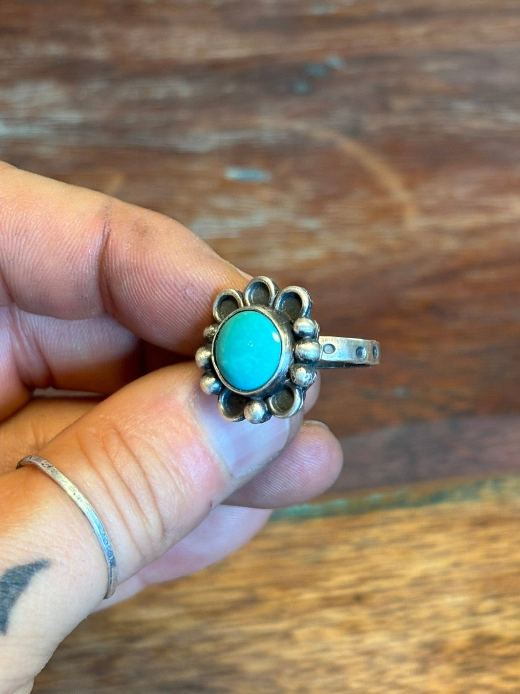 Silver ring with a turquoise stone held by a hand on a wooden surface