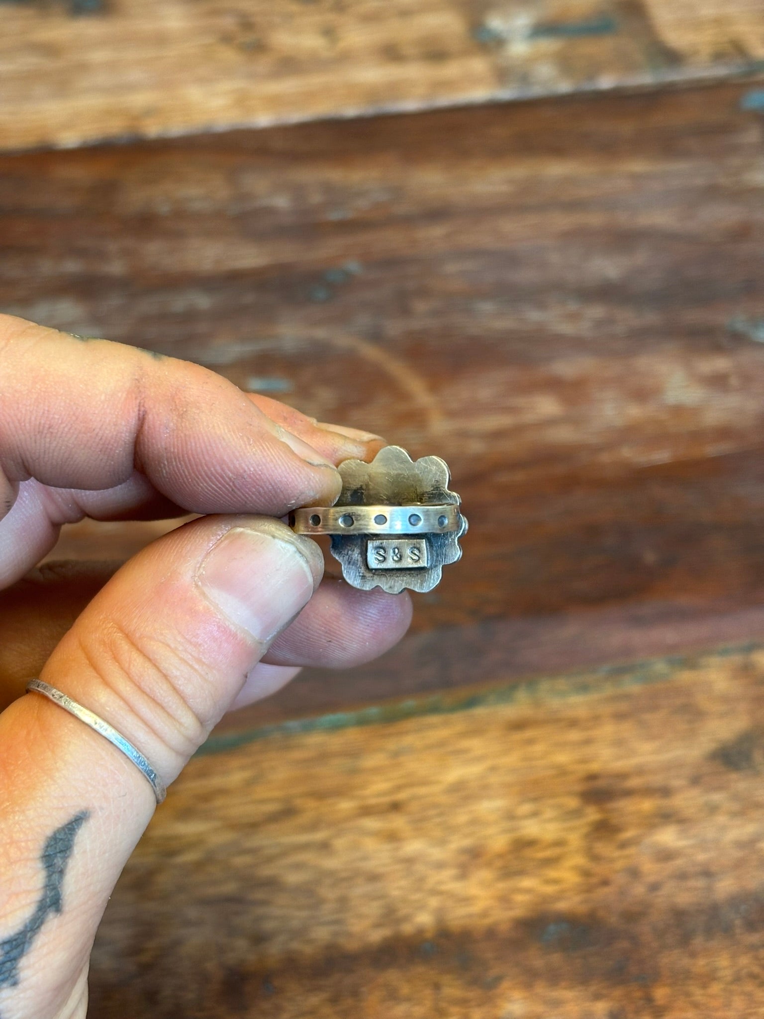 Small ring with a unique design held by a hand against a wooden background