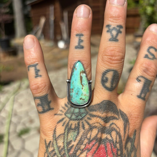 Hand with tattoos wearing a turquoise ring outdoors