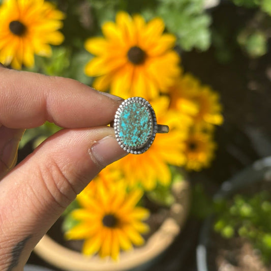 Turquoise ring held up to yellow flowers with a garden background
