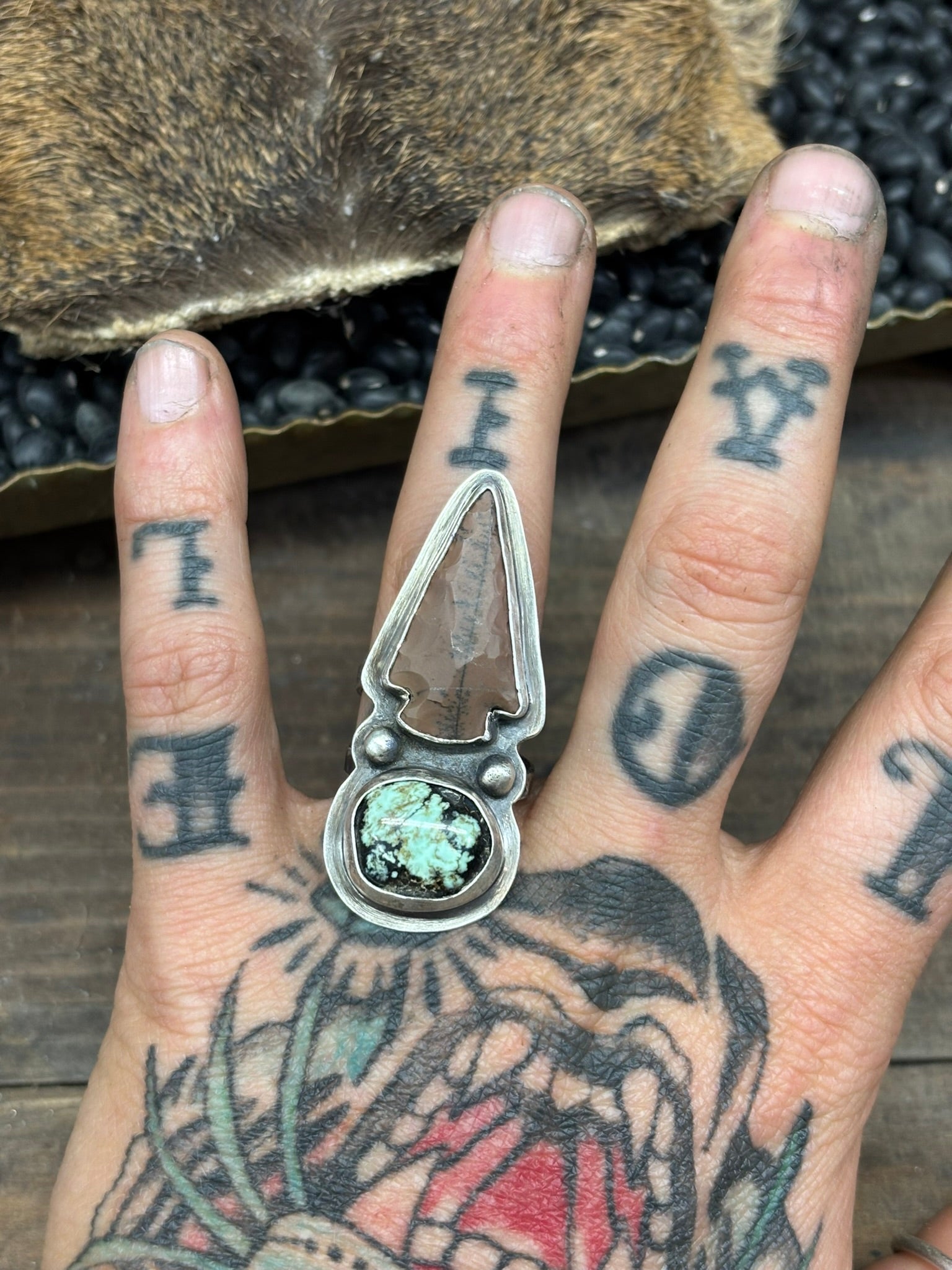 variscite stone and arrowhead ring in sterling and fine silver, handmade and artist signed. shown on ring finger of tattooed hand, tiger teeth
